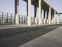 an empty sidewalk that has some columns in it under a blue sky with clouds on the top