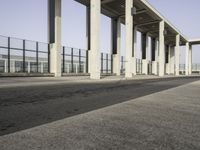 an empty sidewalk that has some columns in it under a blue sky with clouds on the top