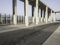 an empty sidewalk that has some columns in it under a blue sky with clouds on the top