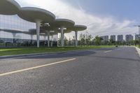 a road lined with silver trees in front of a glass building with tall columns and windows