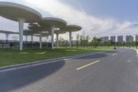 a road lined with silver trees in front of a glass building with tall columns and windows