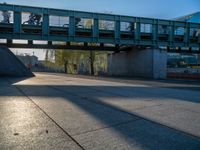 a skateboarder riding on a cement ramp next to a city street under a bridge