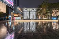 a sidewalk near buildings and a walkway at night with rain in the city center of the picture