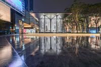 a sidewalk near buildings and a walkway at night with rain in the city center of the picture