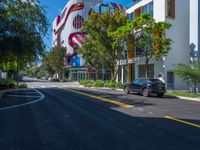 cars are parked in a parking lot in front of a building with a giant american flag