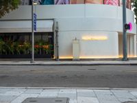 a white building with posters on it on a sidewalk in front of the building is a pink lit sign