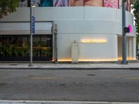 a white building with posters on it on a sidewalk in front of the building is a pink lit sign