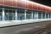 this is a bus stop at night next to the curb of a building with a large mirror window