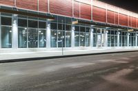 this is a bus stop at night next to the curb of a building with a large mirror window