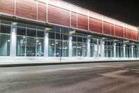 this is a bus stop at night next to the curb of a building with a large mirror window