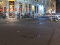 a manhole is seen at the middle of the city intersection at night, with people lined up along it