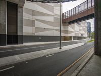 a road runs alongside side of buildings next to a street under an overpass leading to an elevated walkway over a bridge