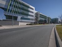 a empty road leads into a building area with glass walls on it and grassy lawn