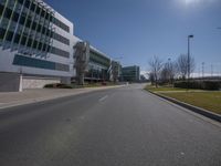 a empty road leads into a building area with glass walls on it and grassy lawn