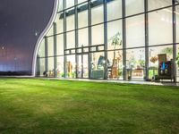 grass in front of a storefront window at night time with the moon overhead and people walking in it