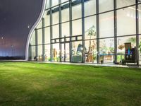 grass in front of a storefront window at night time with the moon overhead and people walking in it