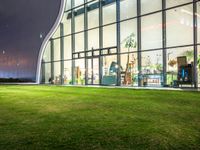 grass in front of a storefront window at night time with the moon overhead and people walking in it