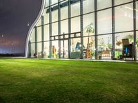 grass in front of a storefront window at night time with the moon overhead and people walking in it