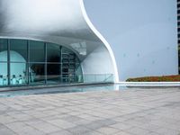 a woman in black top standing on stone walkway next to building with glass windows and curved architecture