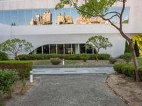 a long white building with glass windows in a courtyard with trees in the foreground