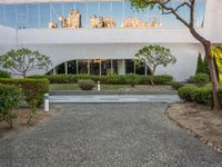 a long white building with glass windows in a courtyard with trees in the foreground