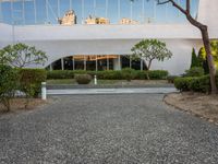 a long white building with glass windows in a courtyard with trees in the foreground