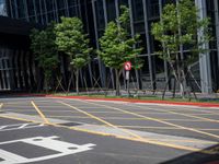 a red stop sign sitting next to some trees and bushes in a parking lot surrounded by tall buildings