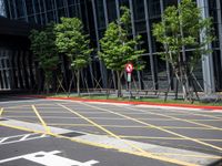 a red stop sign sitting next to some trees and bushes in a parking lot surrounded by tall buildings