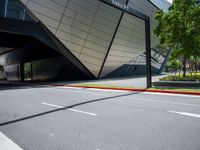 an empty street and sidewalk with a large metallic building in the background of it,