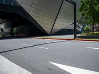 an empty street and sidewalk with a large metallic building in the background of it,