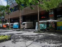 an intersection with trees, shrubs and small trailers parked in front of it and several small vans on either side