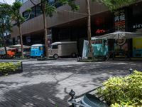 an intersection with trees, shrubs and small trailers parked in front of it and several small vans on either side