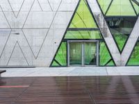 a bench and a wall with geometric glass panels in front of it with someone on a sidewalk walking by it