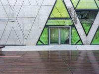 a bench and a wall with geometric glass panels in front of it with someone on a sidewalk walking by it