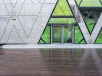 a bench and a wall with geometric glass panels in front of it with someone on a sidewalk walking by it