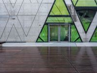 a bench and a wall with geometric glass panels in front of it with someone on a sidewalk walking by it