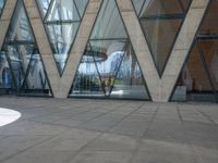 the woman is walking with her umbrella on the sidewalk in front of the building and the reflection in the window