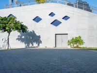 the side of a large building has windows with rounded shapes and trees on either side