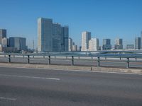 the highway and bridge leading to a city in japan and has tall buildings and blue skies