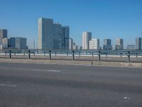 the highway and bridge leading to a city in japan and has tall buildings and blue skies