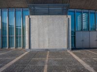 a sidewalk that has several glass doors next to it with buildings in the background behind