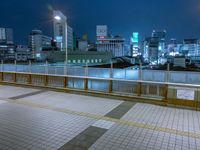 people standing on a subway platform with many buildings in the background at night light in tokyo