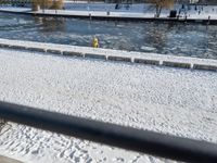 a person sitting on a bench in the snow next to a river and boats docked