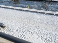 a person sitting on a bench in the snow next to a river and boats docked