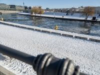 a person sitting on a bench in the snow next to a river and boats docked