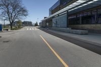 the empty road is lined with empty trees in the front of this building at the end of the street