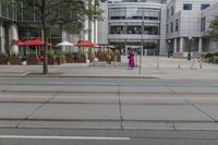 a woman in a pink dress standing on a city street corner holding a cell phone