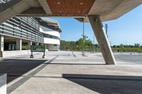 a sidewalk with benches that are under a large bridge to the right of the walkway is a metal frame with concrete columns