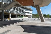 a sidewalk with benches that are under a large bridge to the right of the walkway is a metal frame with concrete columns