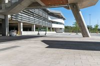 a sidewalk with benches that are under a large bridge to the right of the walkway is a metal frame with concrete columns